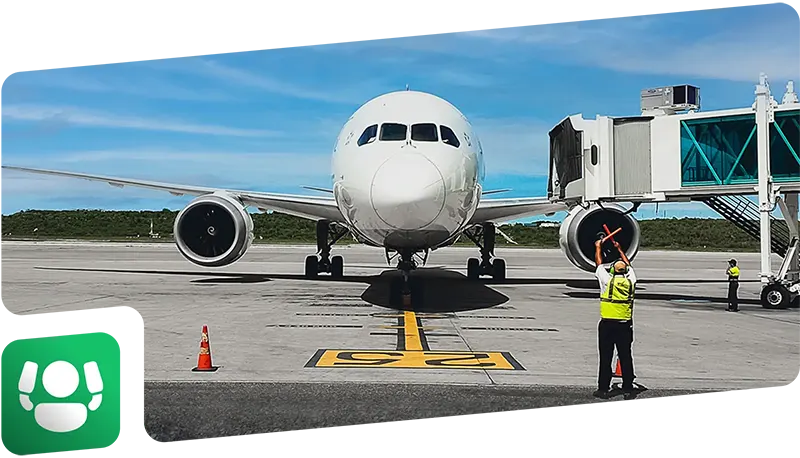 Avión de color blanco visto de frente, siendo guiado a un lugar de estacionamiento por un operador